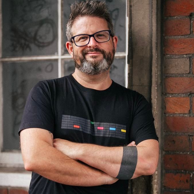 Howard Scott, photographed against a brick wall, arms folded, looking to camera